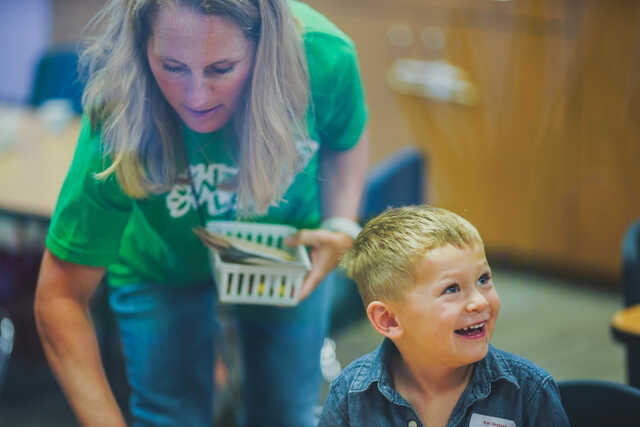 Volunteer giving art supplies to a very happy preschooler